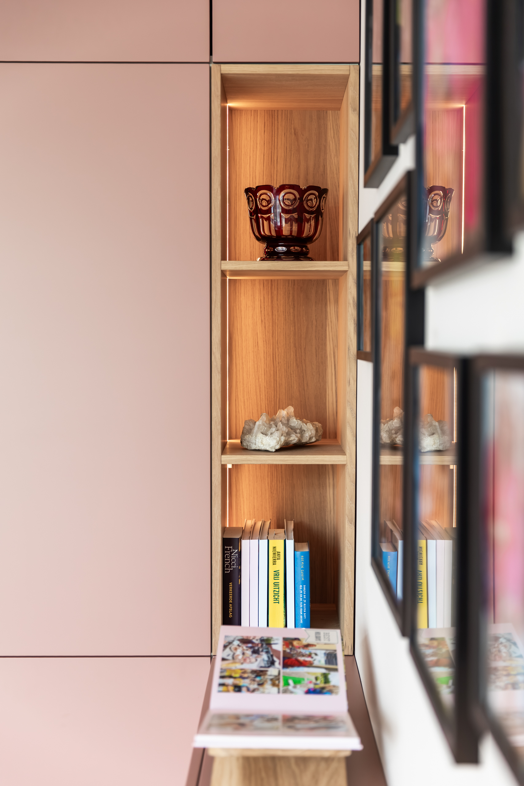 Verlichte eiken nis met glaswerk en boeken in de terra-roze maatwerkkast, interieurontwerp woning Bennebroek